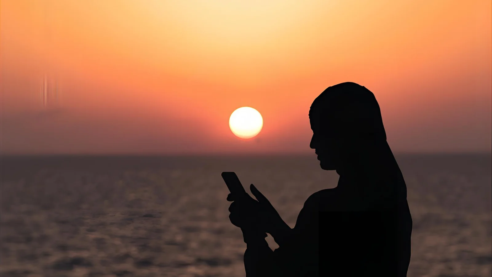 Wide sunset over the ocean with a silhouetted person holding a phone, horizon glowing orange and pink, soft Instagram-style color grading.”